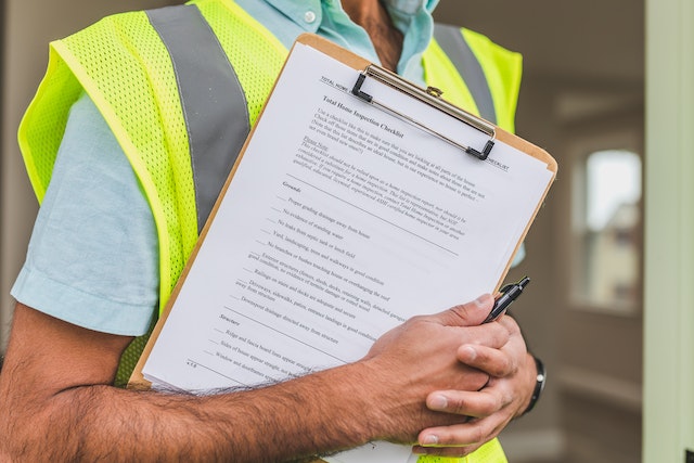 person in yellow reflective vest holding a clipboard with a home inspection checklist on it